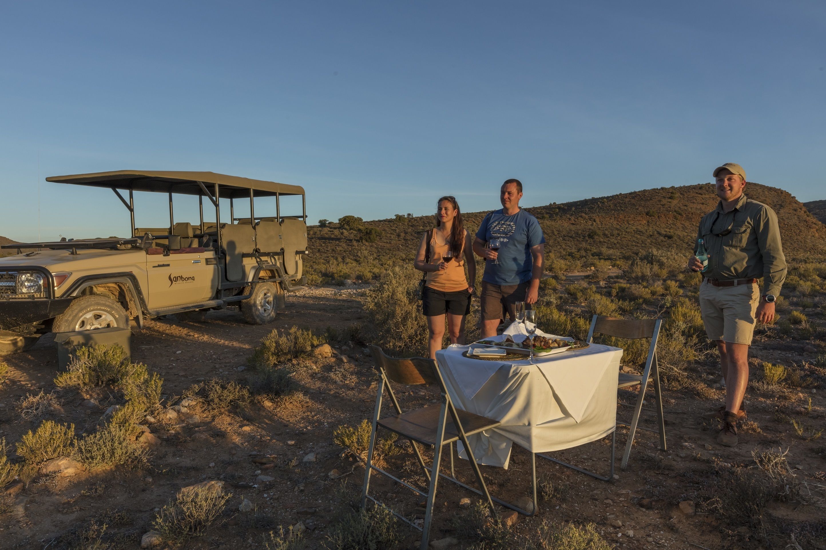 A safari vehicle and a dining setup in a dry, open landscape.