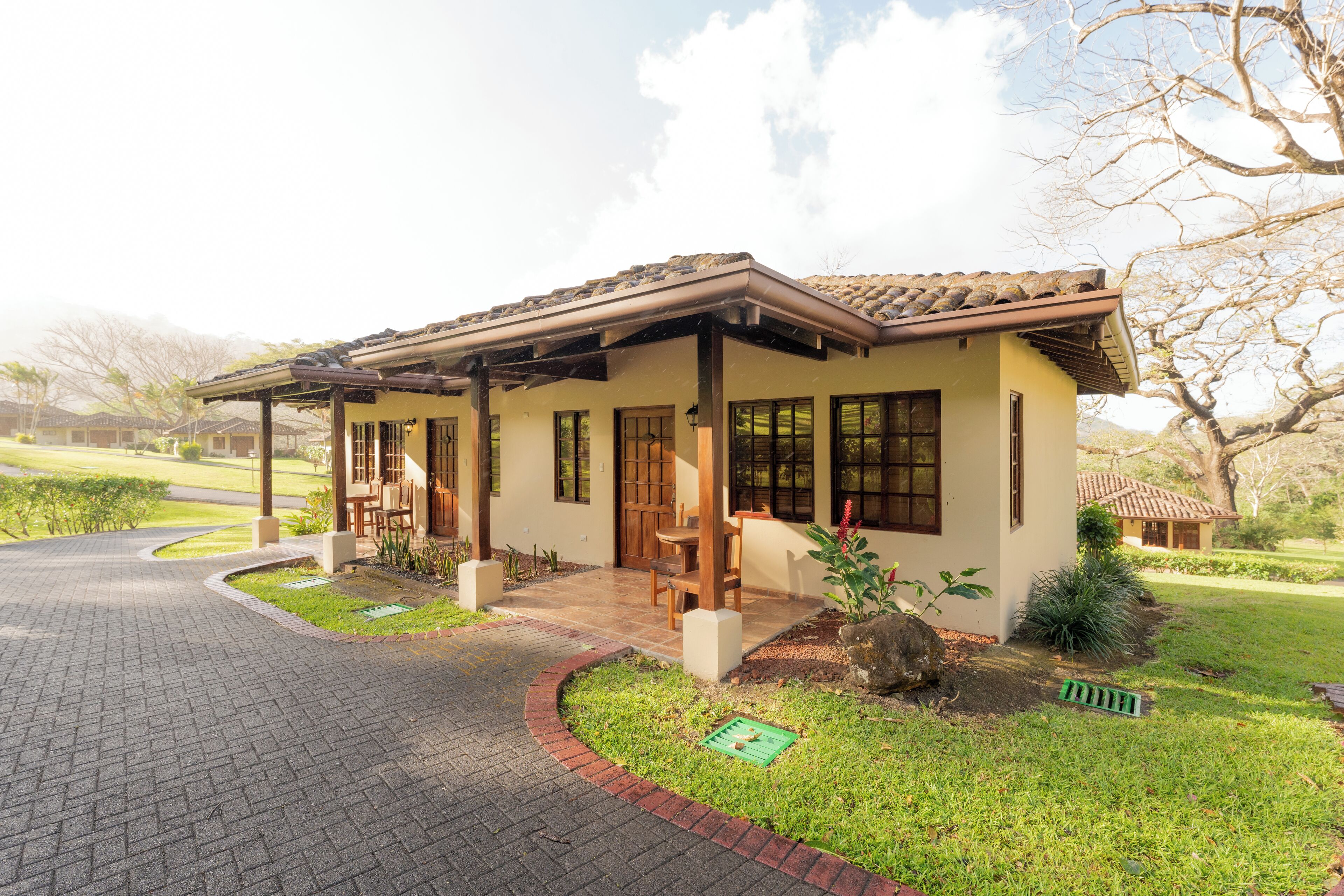 Uma casa com varanda, um pequeno jardim e um caminho de entrada calçado.