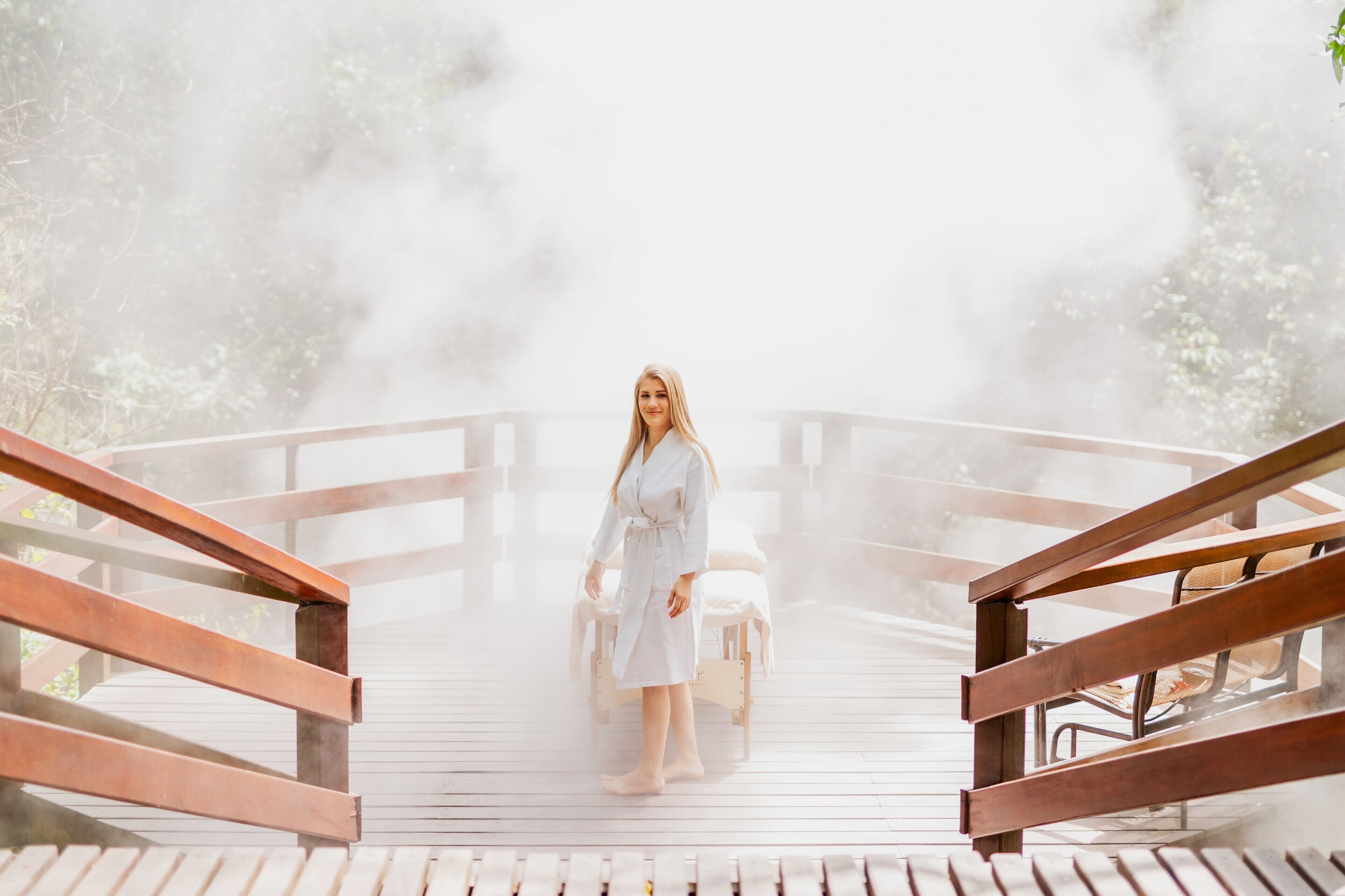 A wooden deck with a person in a white robe standing in the center, surrounded by steam.