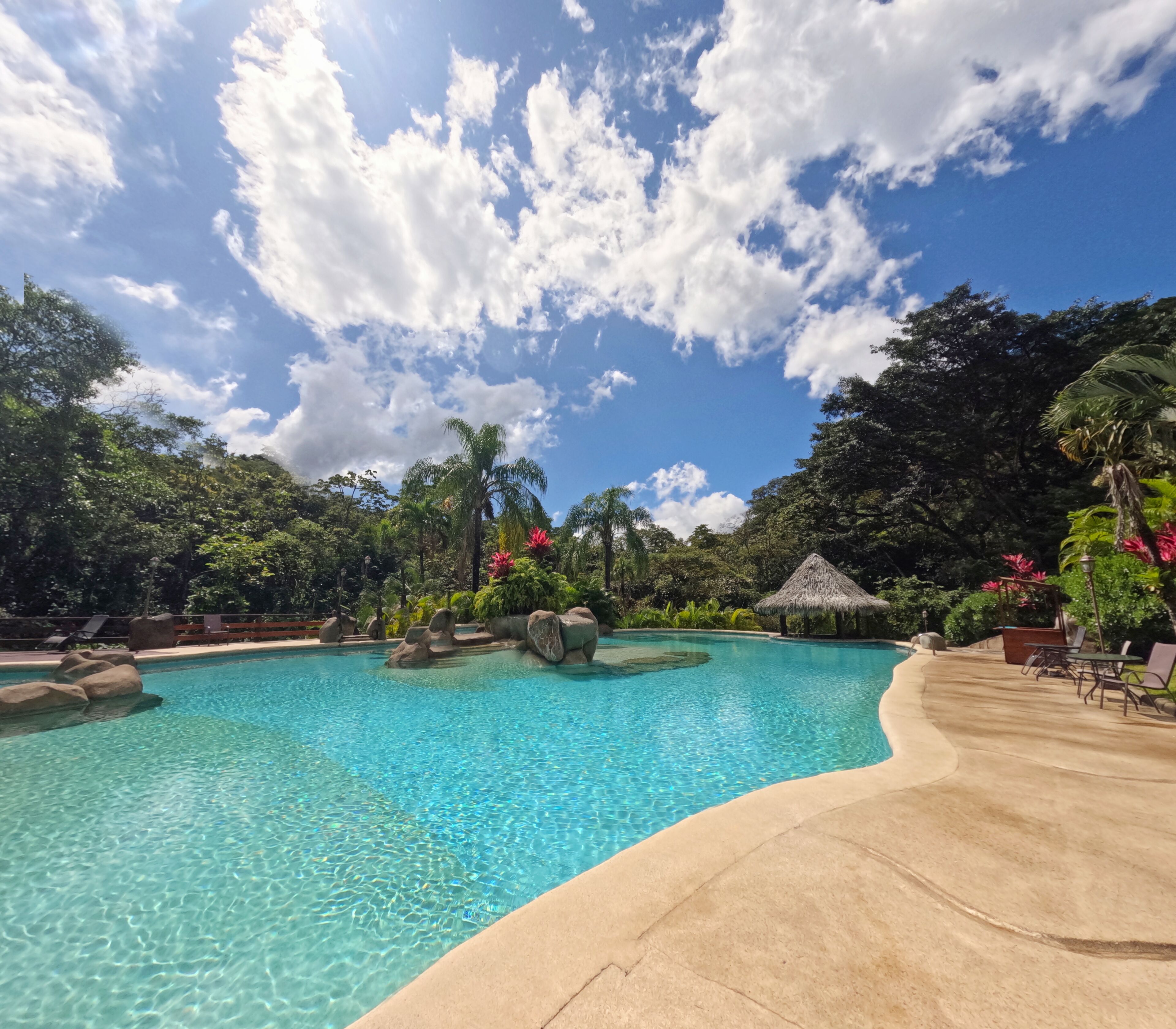 Una piscina azul cristalina rodeada de follaje tropical y una estructura con techo de paja.