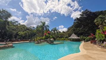 Una piscina azul cristalina rodeada de follaje tropical y una estructura con techo de paja.