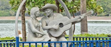 Una escultura de un hombre y una mujer sentados bajo un arco circular, con una guitarra entre ellos.