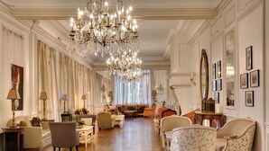 A spacious living room with a grand chandelier, elegant furniture, and a large mirror. - Pavillon Henri IV Hotel Restaurant Gastronomique Terrasse (Saint-Germain-en-Laye)