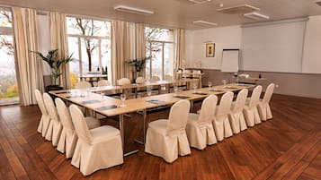 Une salle de conférence équipée d’une longue table, de chaises, d’un écran de projection et de grandes fenêtres avec des rideaux.