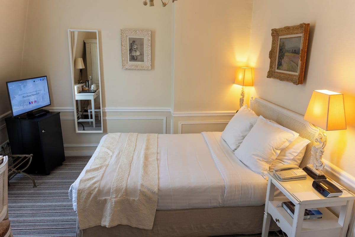 A hotel room with a bed, bedside table, lamp, and a TV on a desk.