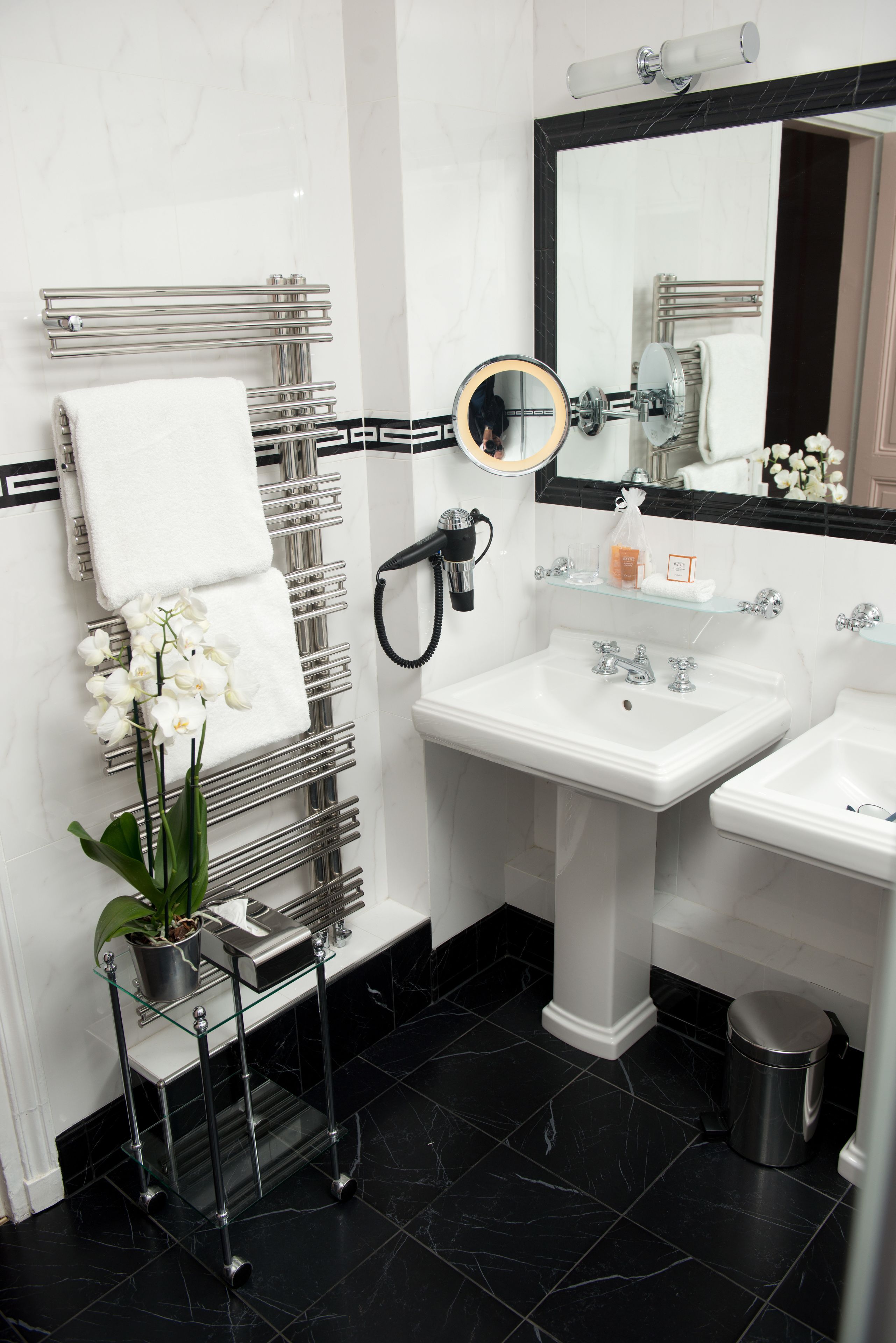 A modern bathroom with a black and white tiled floor, a white sink, a mirror with a round frame, and a towel rack with white towels.