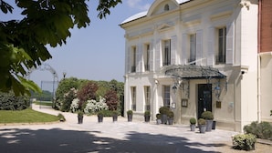 A classical building with a symmetrical facade, a central entrance with a canopy, and a well-maintained garden with potted plants and a fountain. - Pavillon Henri IV Hotel Restaurant Gastronomique Terrasse (Saint-Germain-en-Laye)