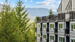 A multi-story building with balconies, large windows, and a mountainous backdrop.
