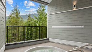 A balcony with a hot tub, a metal railing, and a view of trees and mountains.