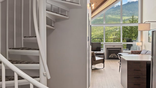 A modern interior with a spiral staircase, a fireplace, and a large window offering a mountain view.