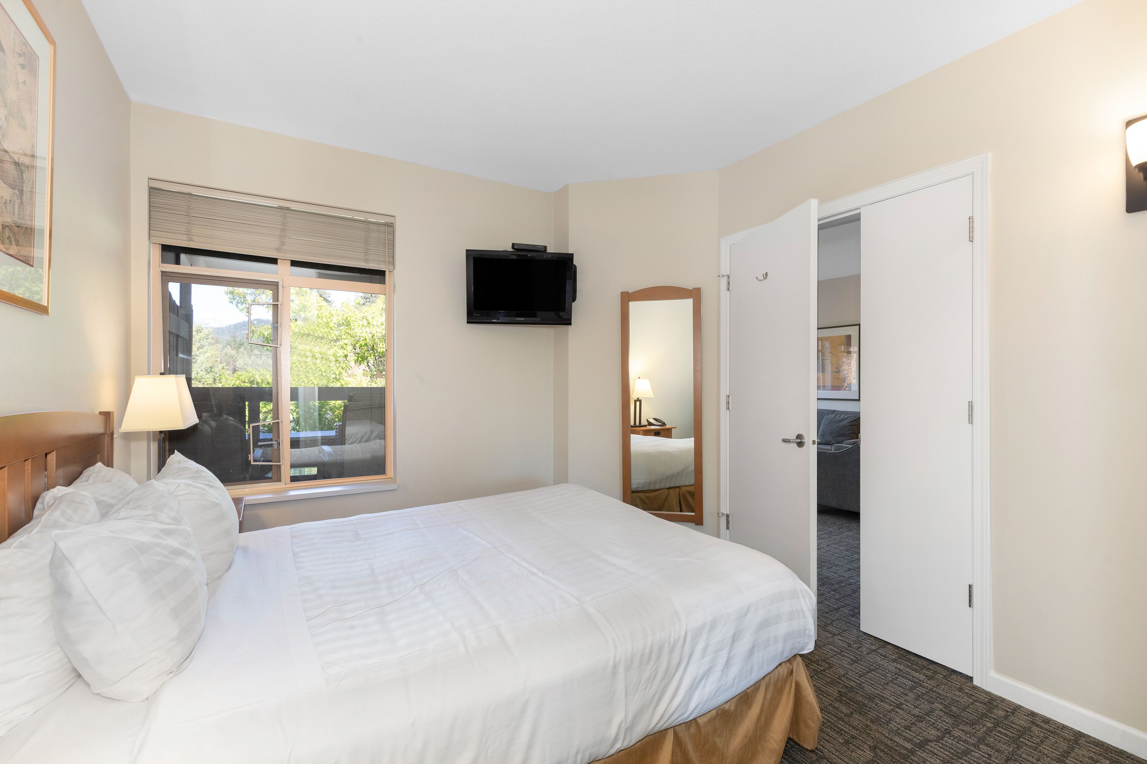 A hotel room with a bed, a television, a window with blinds, and a door leading to another room.