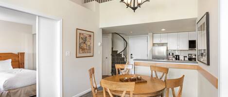 A hotel room with a bed, a dining table with chairs, a kitchen area, and a staircase.