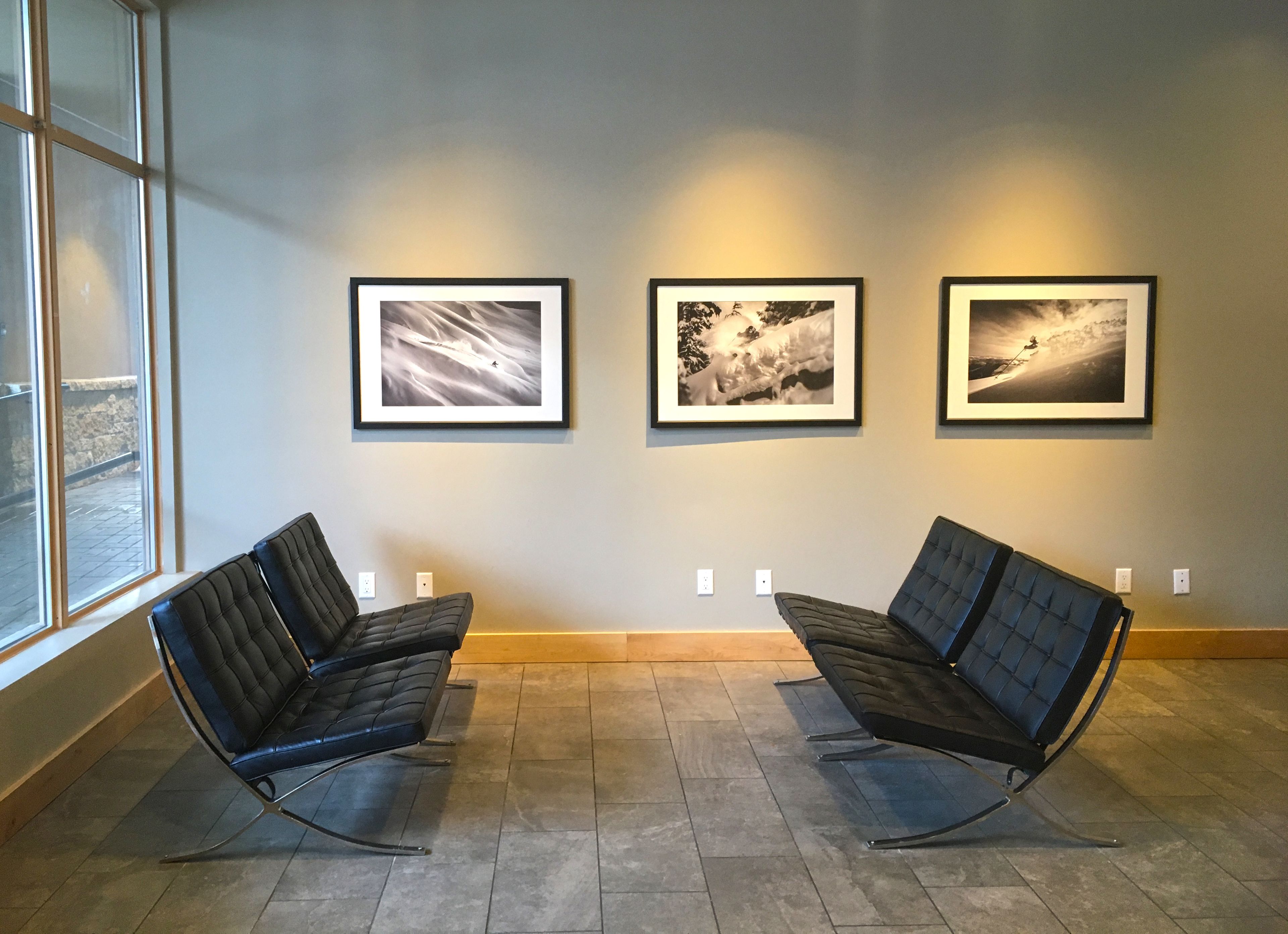 A waiting area with two black chairs and three framed photographs on the wall.