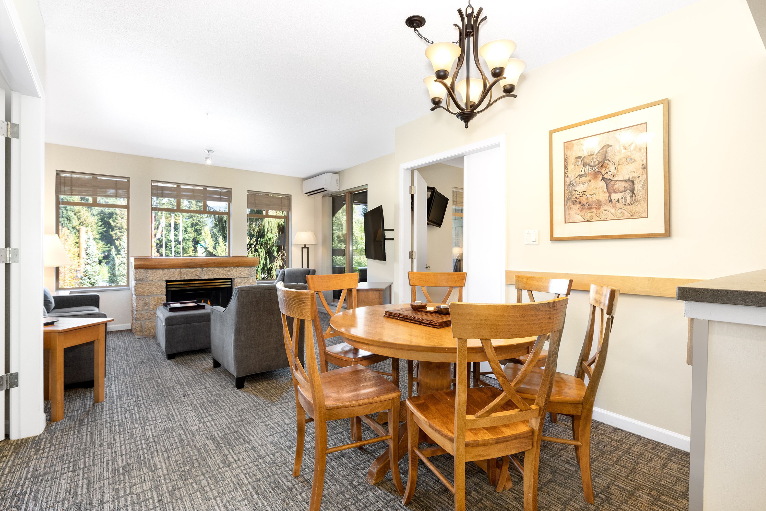 A dining area with a round wooden table and chairs, a chandelier, and a framed picture on the wall.