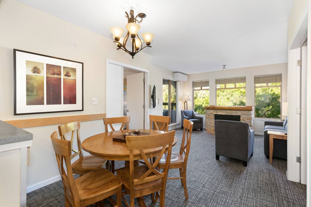 A dining area with a round wooden table and chairs, a chandelier, and a fireplace.