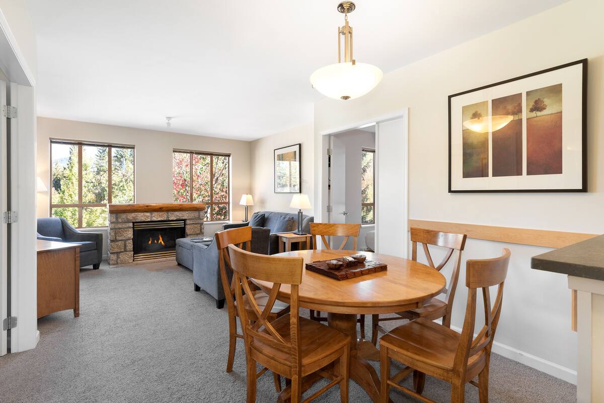 A cozy living room with a fireplace, a dining table with chairs, and a sofa.