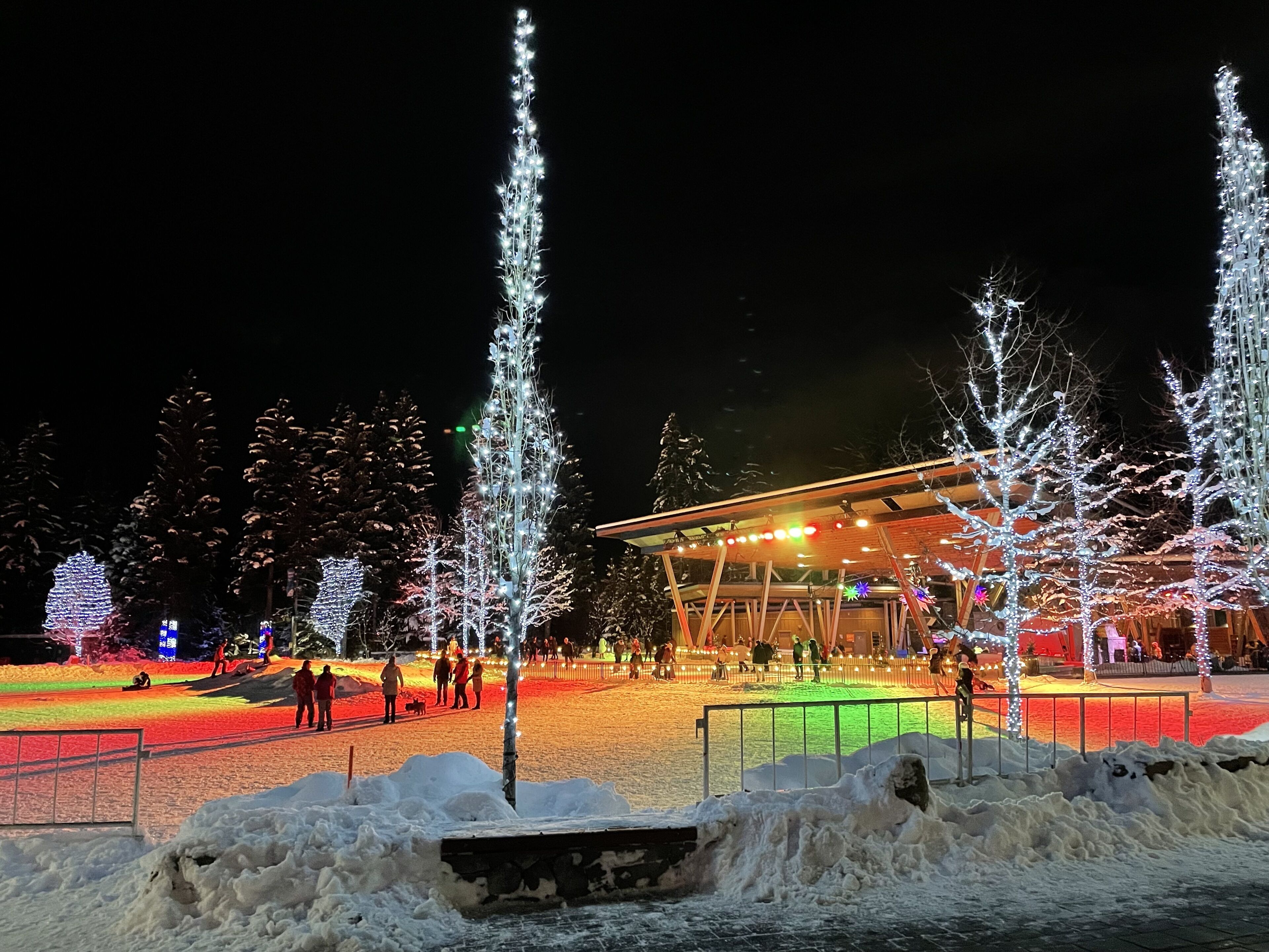 Een sneeuwbedekt plein met verlichte bomen en een gebouw met een glazen gevel.