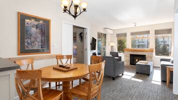 A spacious living room with a fireplace, a dining area with wooden chairs, and large windows allowing natural light.