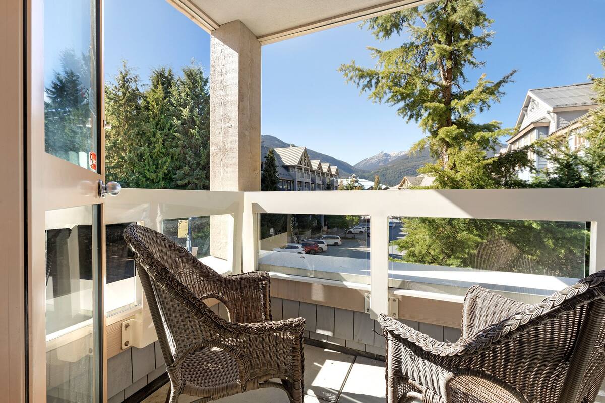 A balcony with wicker chairs, a view of a street, and surrounding trees.