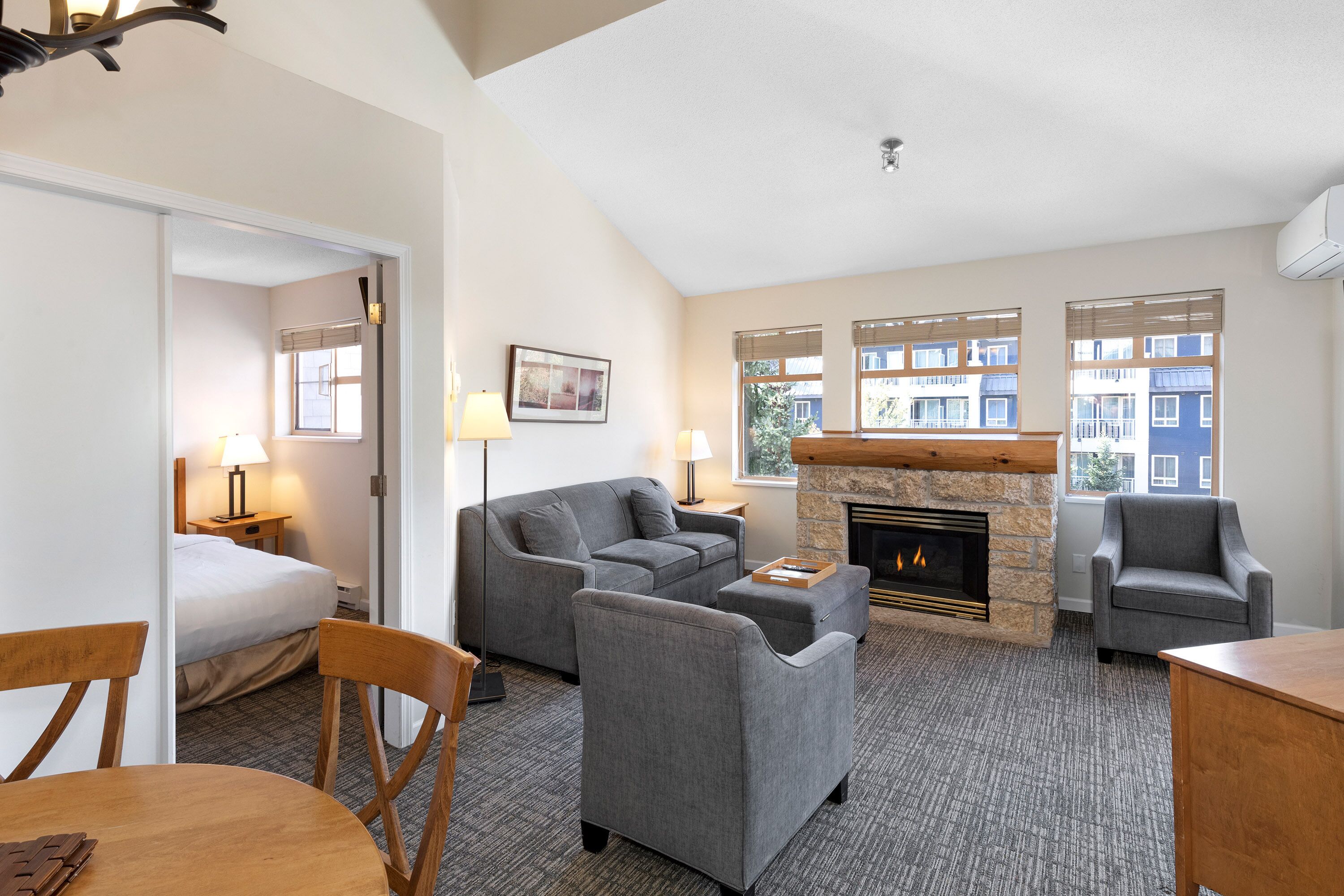 A hotel room with a sofa, armchair, and a fireplace. There is a bed in the corner and a table with chairs.