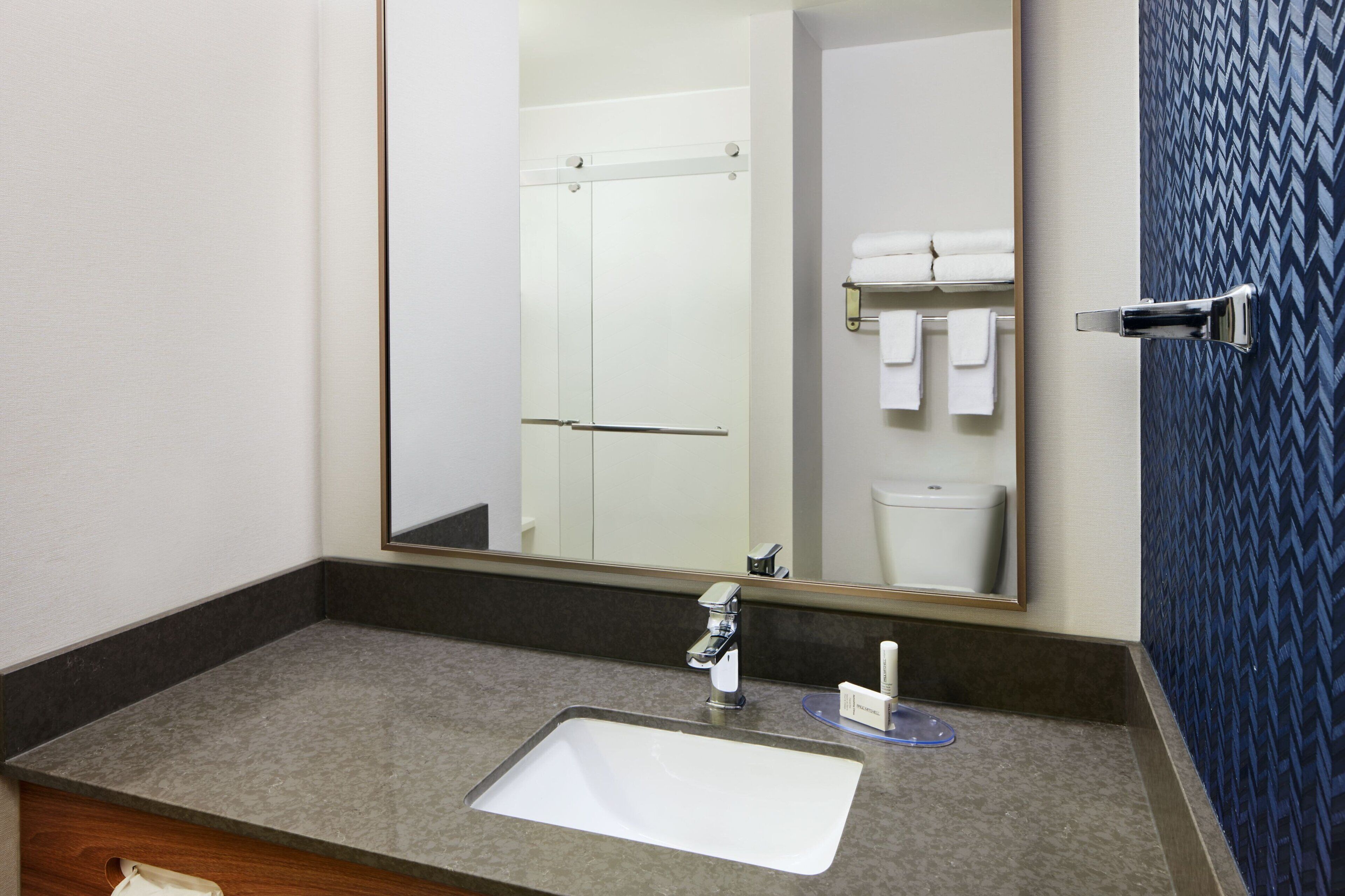 Baño con lavamanos blanco, espejo y puerta de ducha.