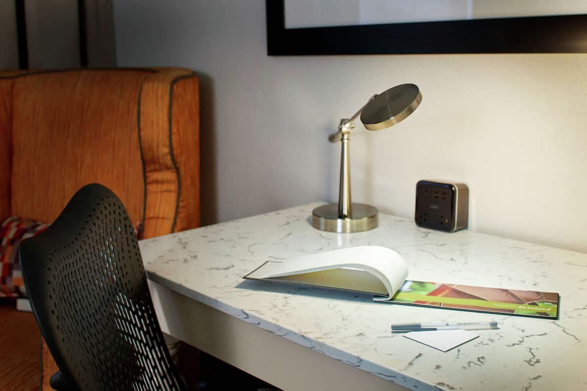 A workspace with a desk, a chair, a desk lamp, a book, a pen, and a remote control.