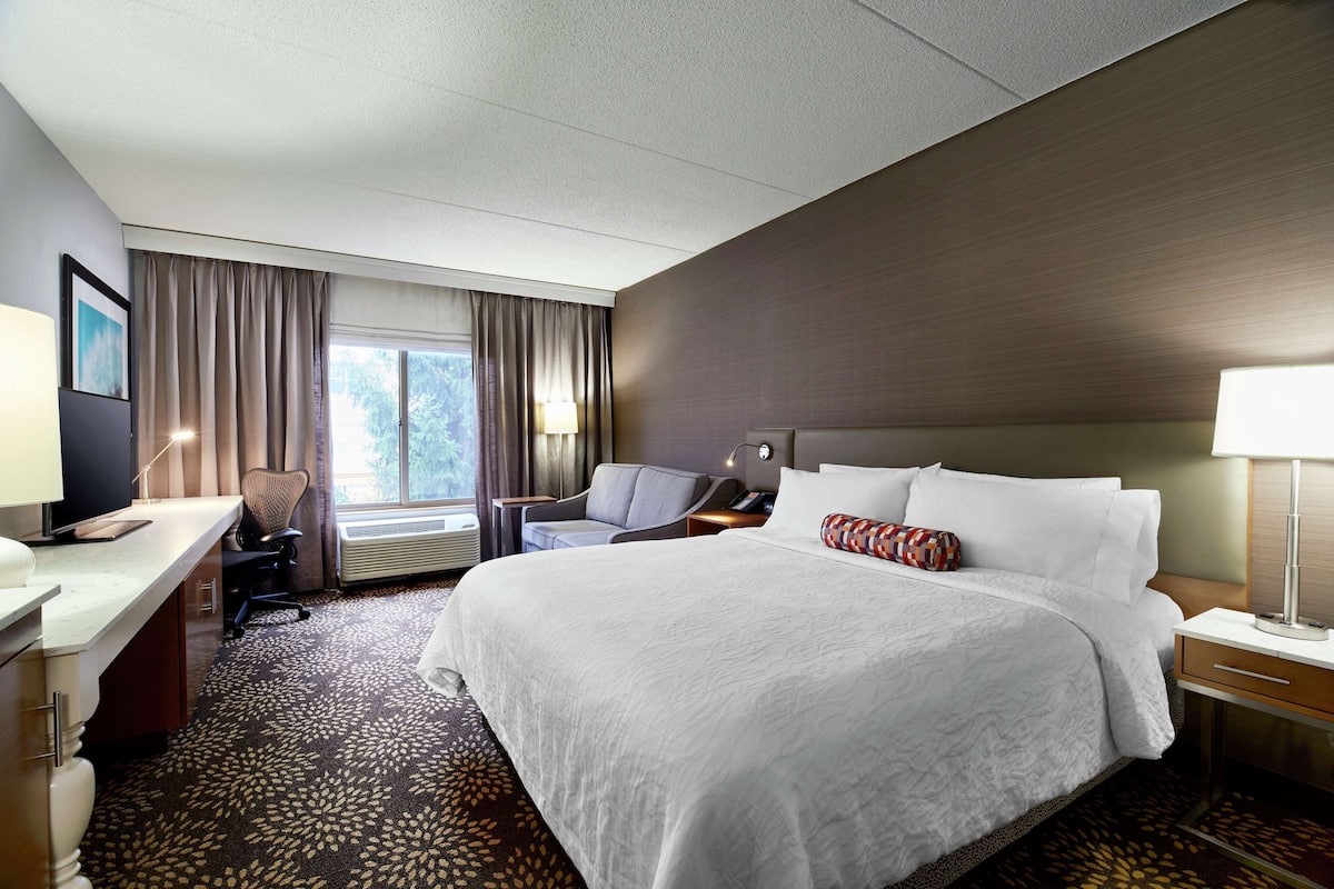 A hotel room with a large bed, a desk, a chair, a TV, and a window with curtains.