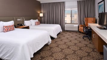 A hotel room with two beds, a desk, a chair, a TV, and a window with curtains.