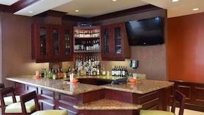 A bar area with a granite countertop, multiple liquor bottles, a flat-screen TV, and bar stools.