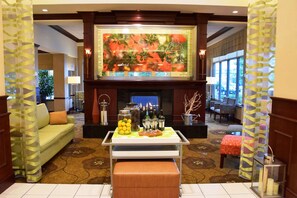 A lobby with a fireplace, a sofa, a table with food and drinks, and a large painting above the fireplace. - Hilton Garden Inn Columbus/Polaris (Columbus)