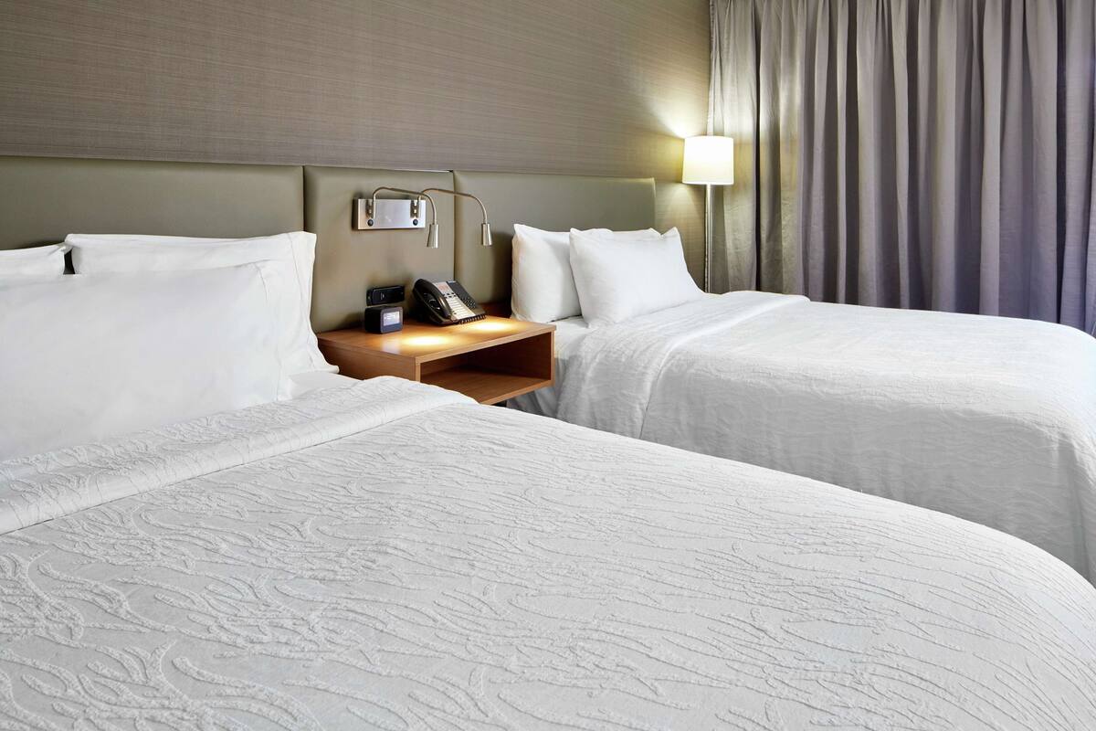 A hotel room with two beds, a bedside table with a lamp, and a telephone.