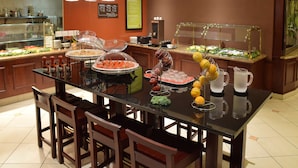 A buffet setup with various food items and a pitcher of water on a glass table.