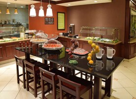 Disposição de buffet com diversos alimentos e uma jarra de água em uma mesa de vidro.