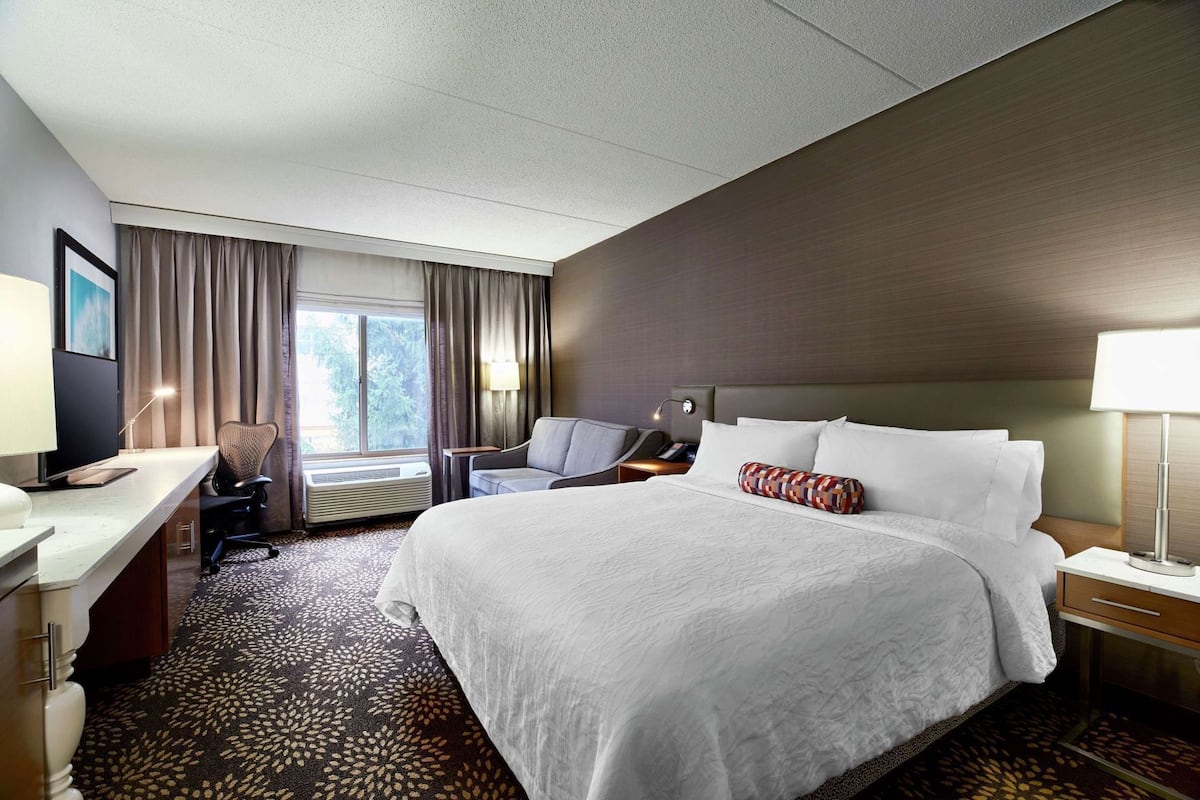 Habitación de hotel con una cama grande, un escritorio con ordenador, una silla, una lámpara y una ventana con cortinas.