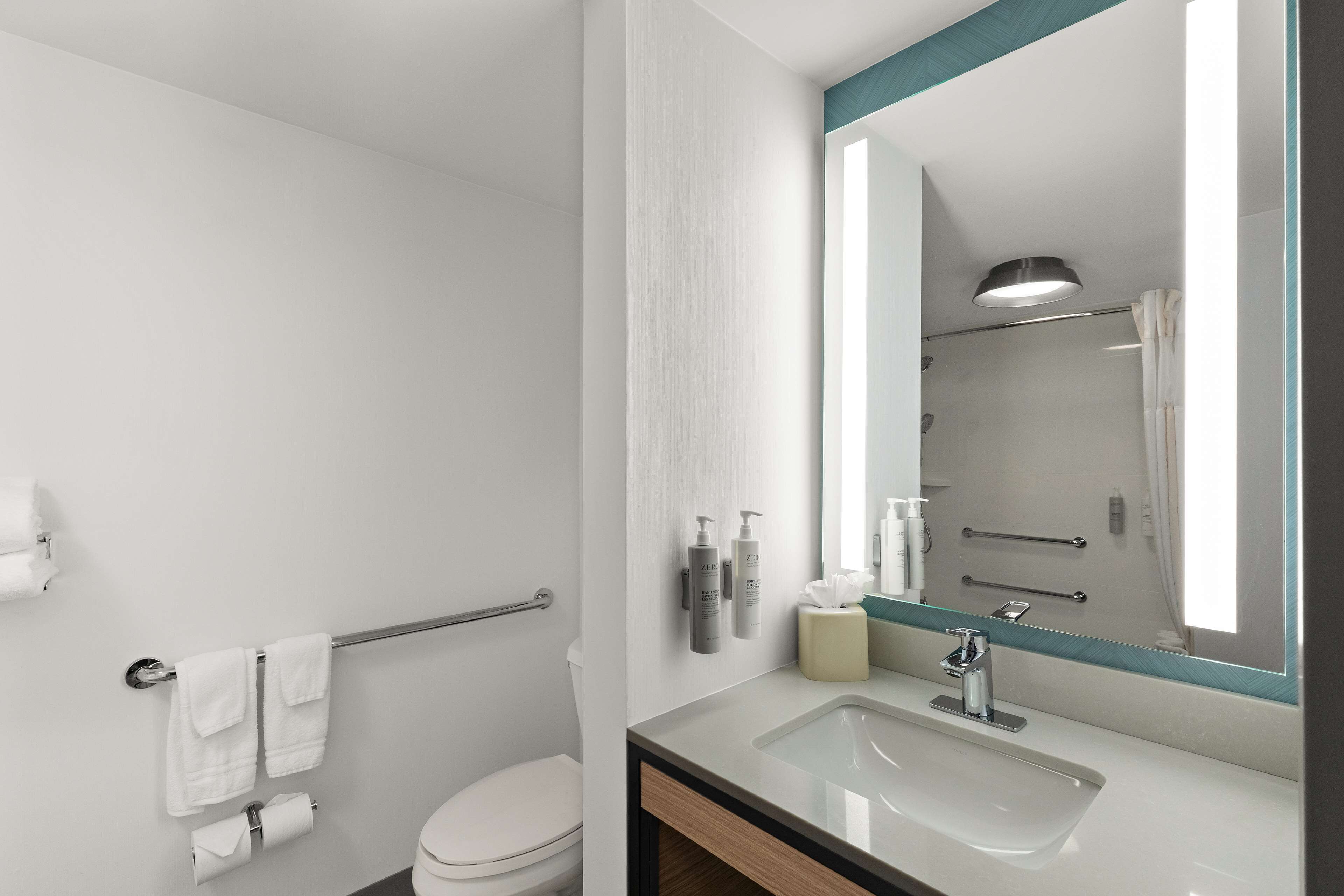 Un baño moderno con un lavabo blanco, un espejo grande y una cabina de ducha de vidrio.