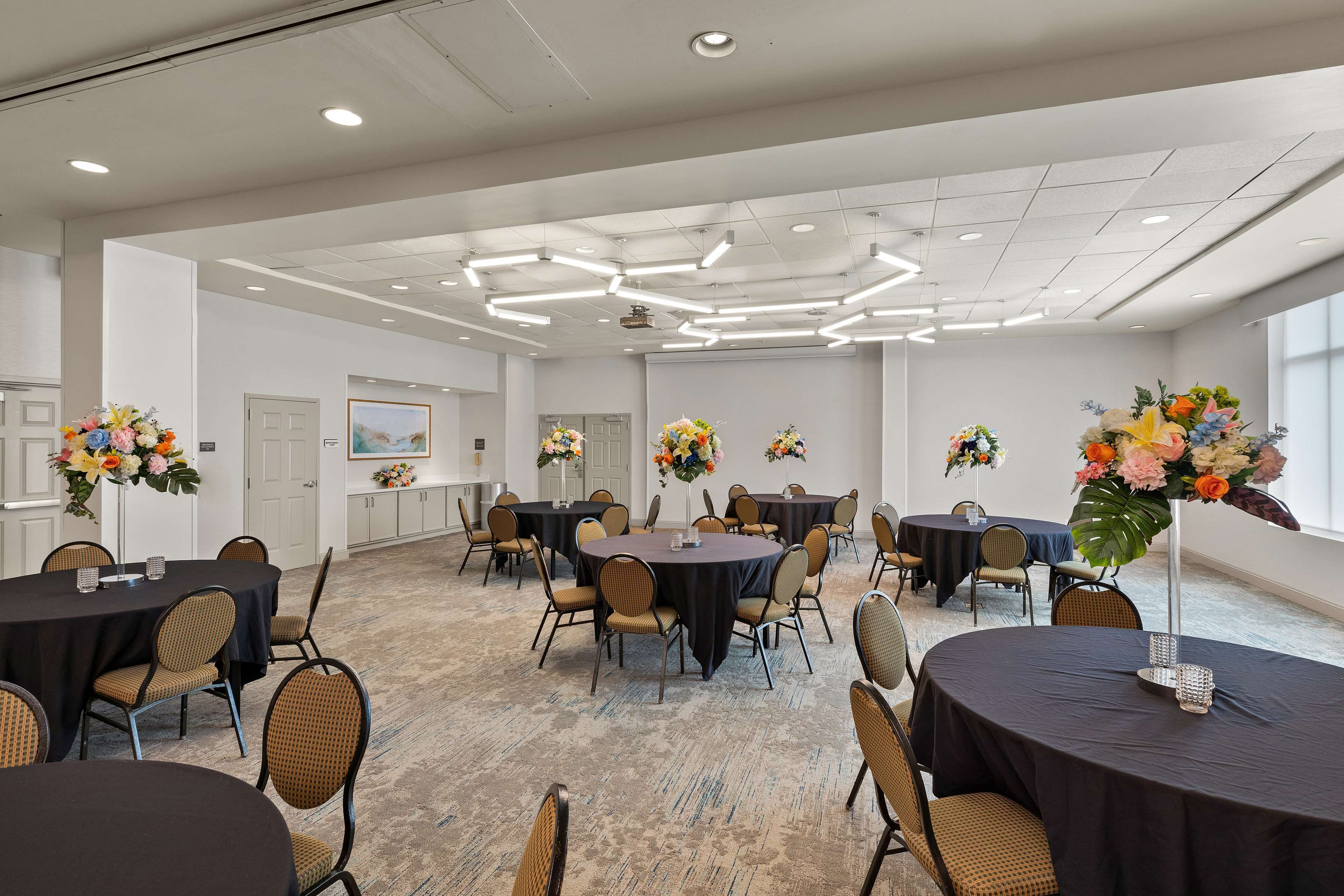 A spacious conference room with multiple round tables, chairs, and floral centerpieces.