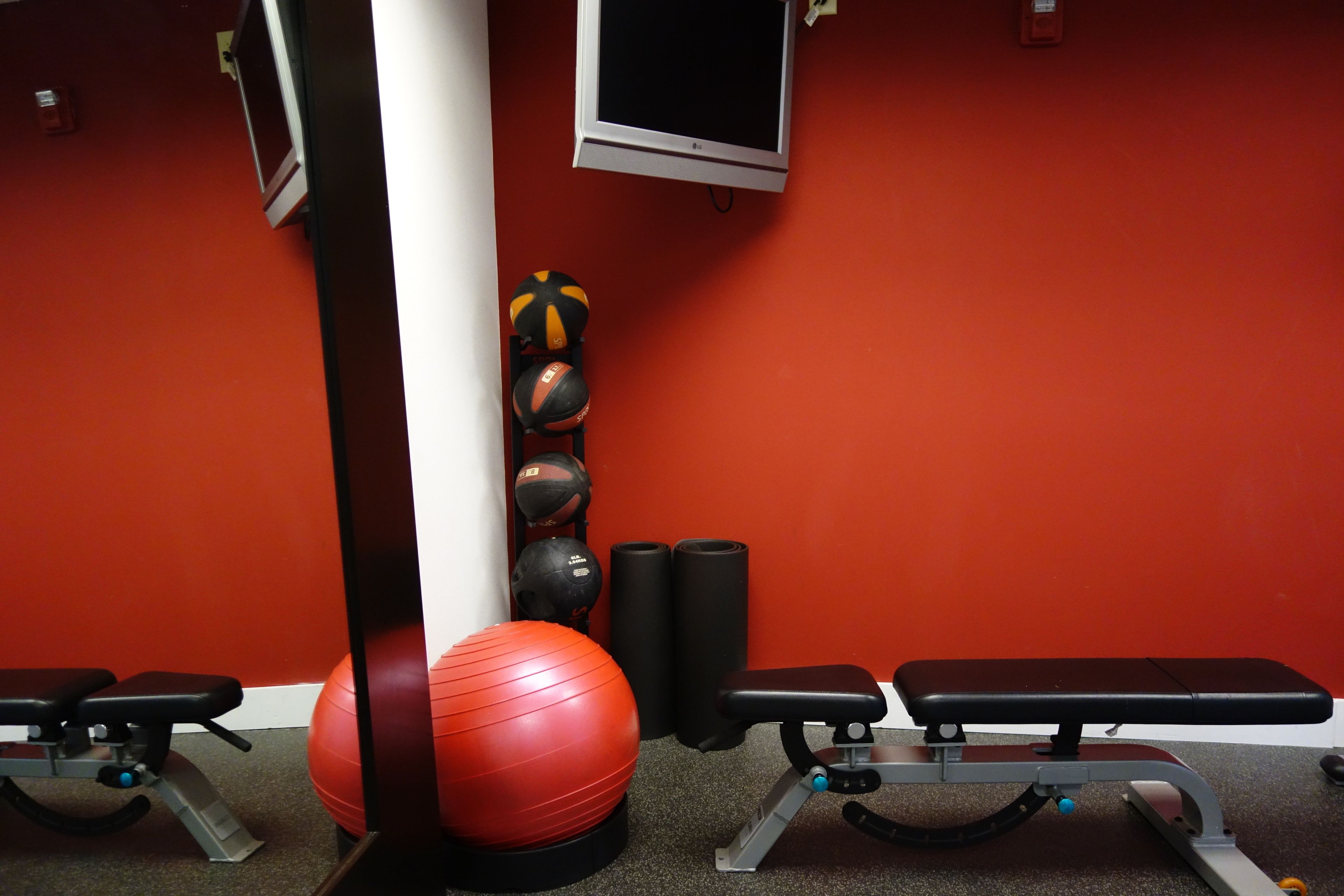 A gym with exercise equipment, a red exercise ball, and a television on the wall.