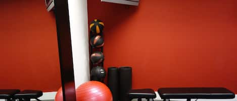 A gym with exercise equipment, a red exercise ball, and a television on the wall.