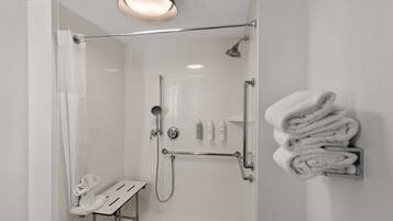 A modern shower area with a glass door, a towel rack with folded towels, and a metal grab bar.
