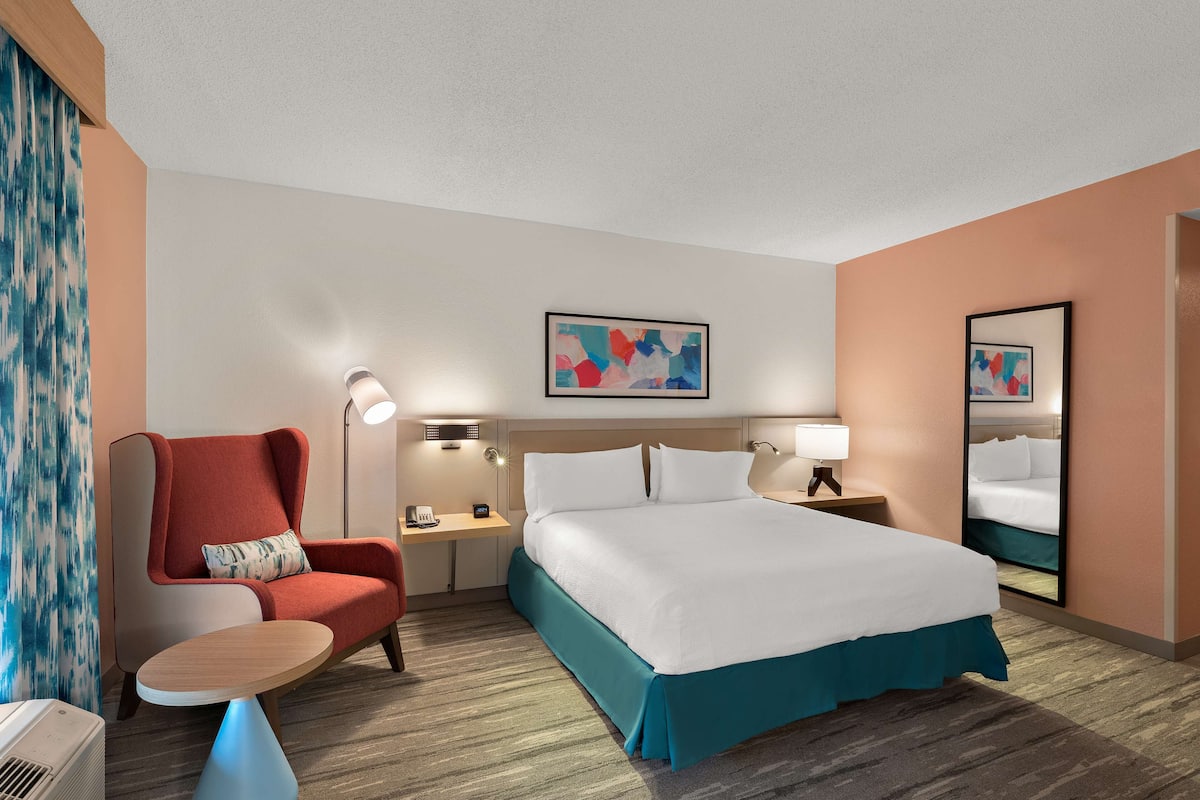 A hotel room with a bed, a chair, a desk, and a mirror.