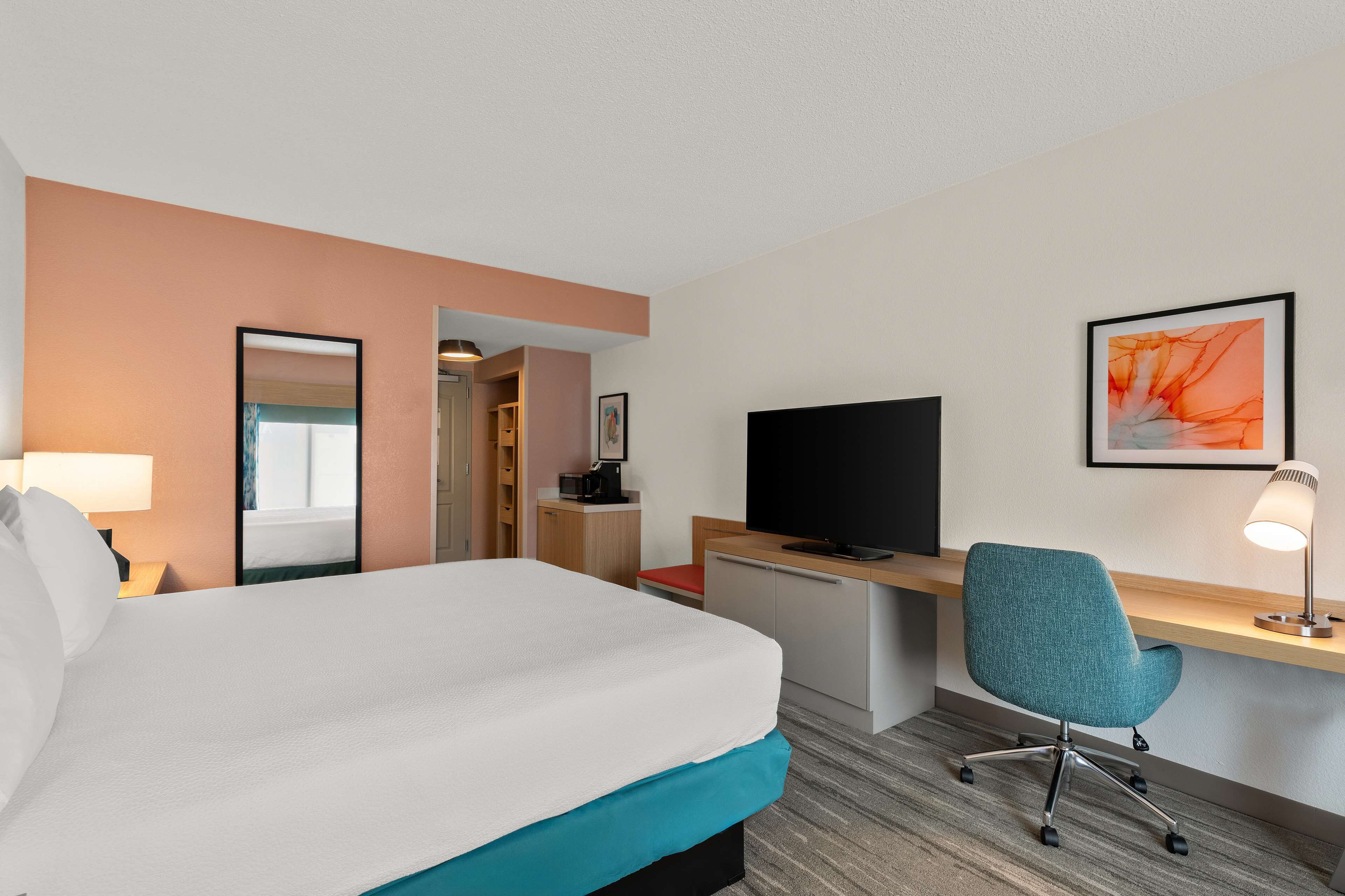 A hotel room with a bed, desk, chair, TV, and a framed picture on the wall.