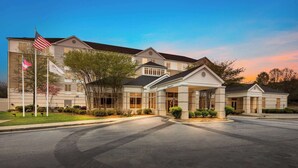 A large, multi-story hotel with a prominent American flag and a covered entrance. - Hilton Garden Inn Atlanta East/Stonecrest (Lithonia)