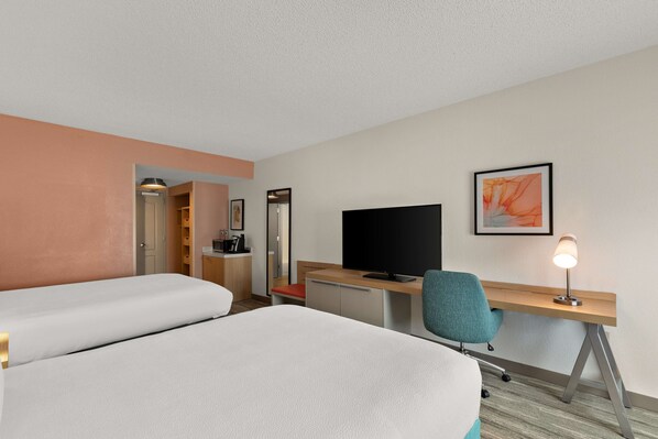 A hotel room with two beds, a desk with a computer, a TV, a chair, and a desk lamp.
