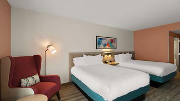 A hotel room with two single beds, a red armchair, a small table, a lamp, and a painting on the wall.