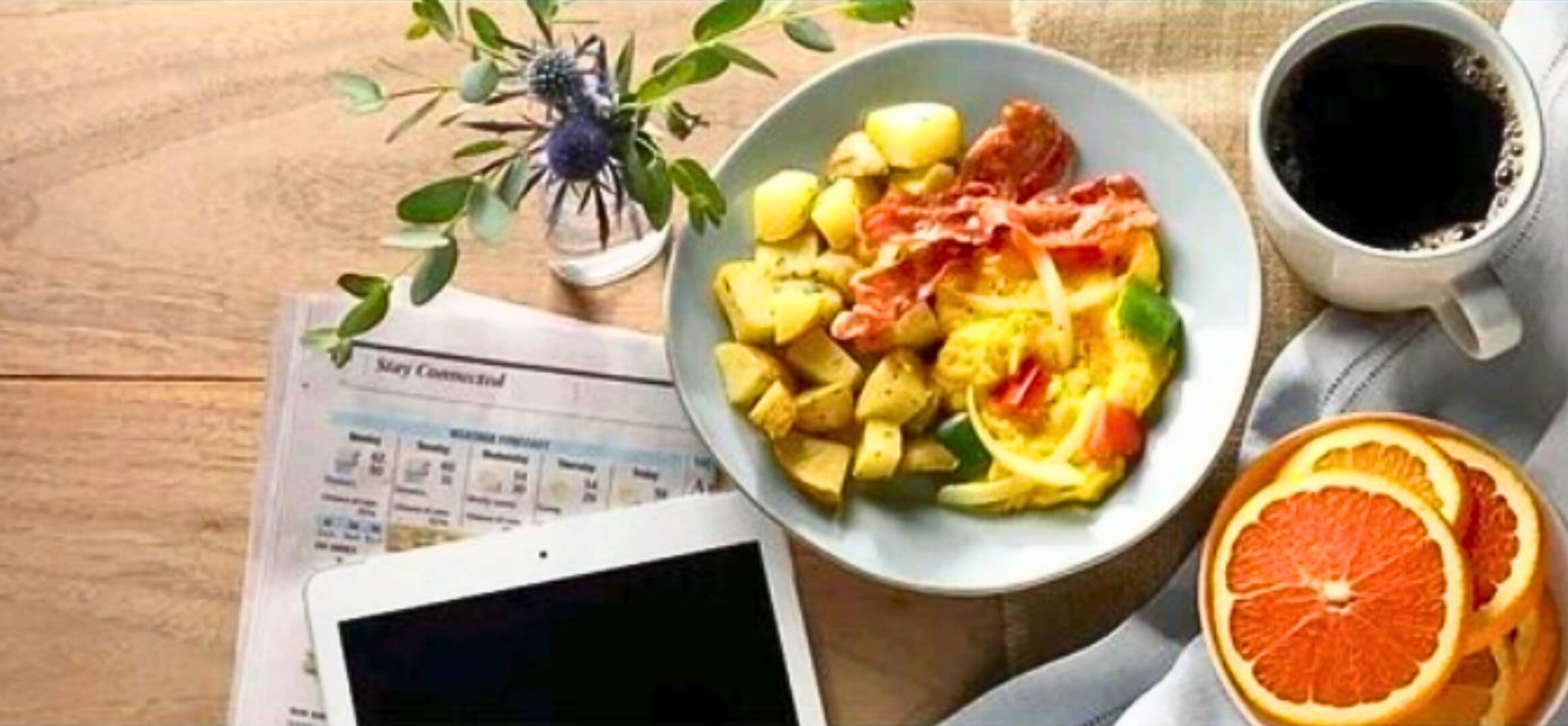 Ein Frühstückstisch mit einer Schüssel Essen, einer Tasse Kaffee, einem Tablet und einem Buch.