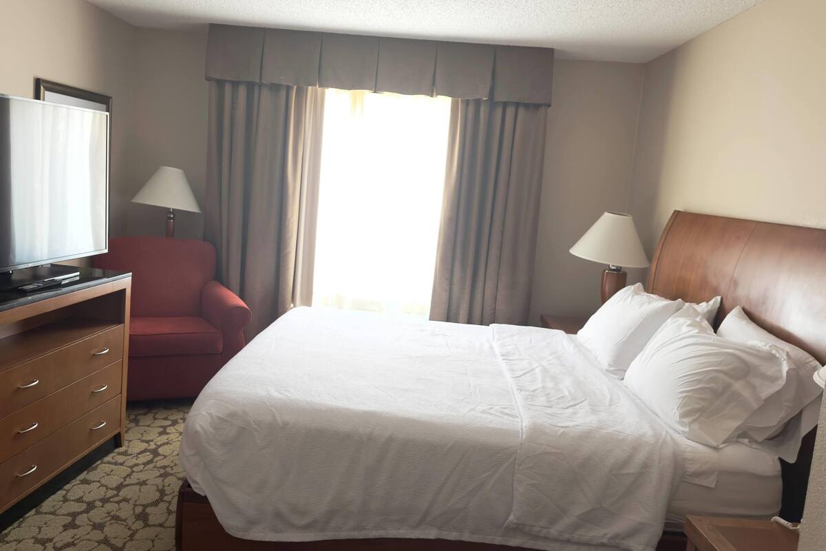 Een hotelkamer met een bed, televisie, bureau, stoel en een raam met gordijnen.