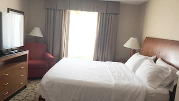 Habitación de hotel con cama, televisión, escritorio, silla y ventana con cortinas.
