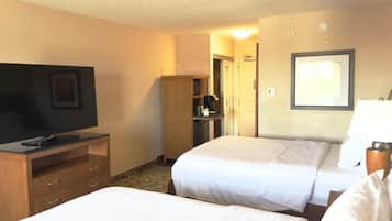 Quarto de hotel com televisão sobre um aparador de madeira, duas camas com lençóis brancos, um guarda-roupa de madeira e um quadro emoldurado na parede.