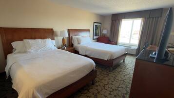 A hotel room with two beds, a desk, a chair, a TV, and a window with curtains.