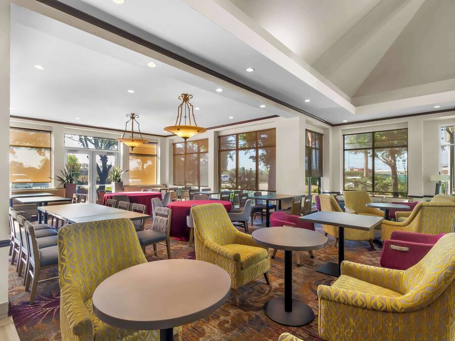 A spacious indoor area with multiple tables and chairs, large windows, and ceiling lights.